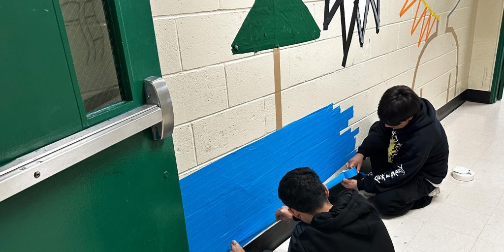 Two students in a hallway using Pro Tapes blue masking tape to create tape art. 