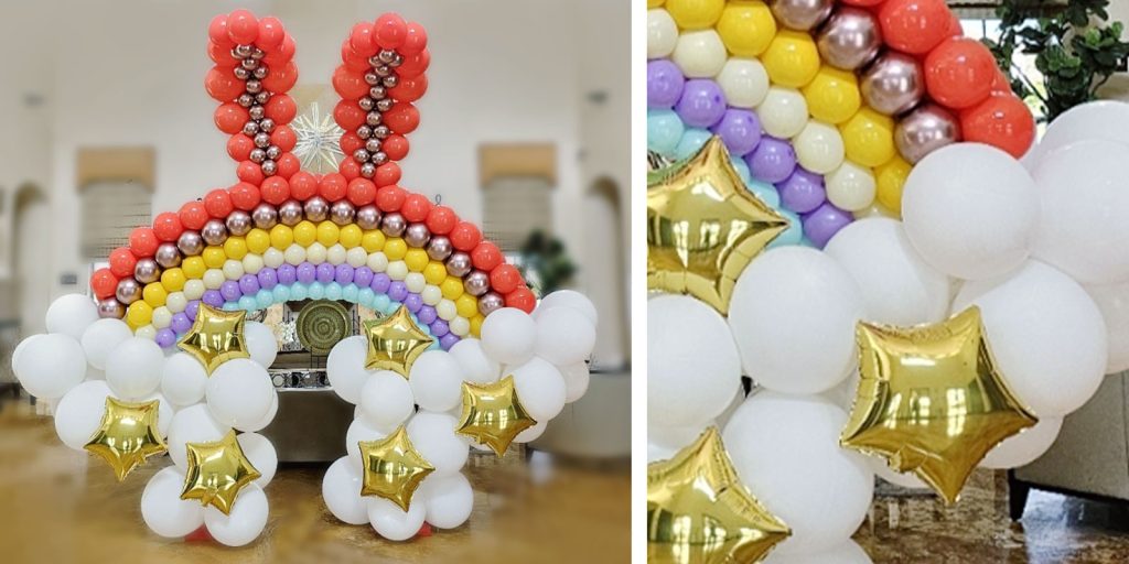 A large colorful rainbow arch with bunny ears and gold star balloons for an easter celebration. 